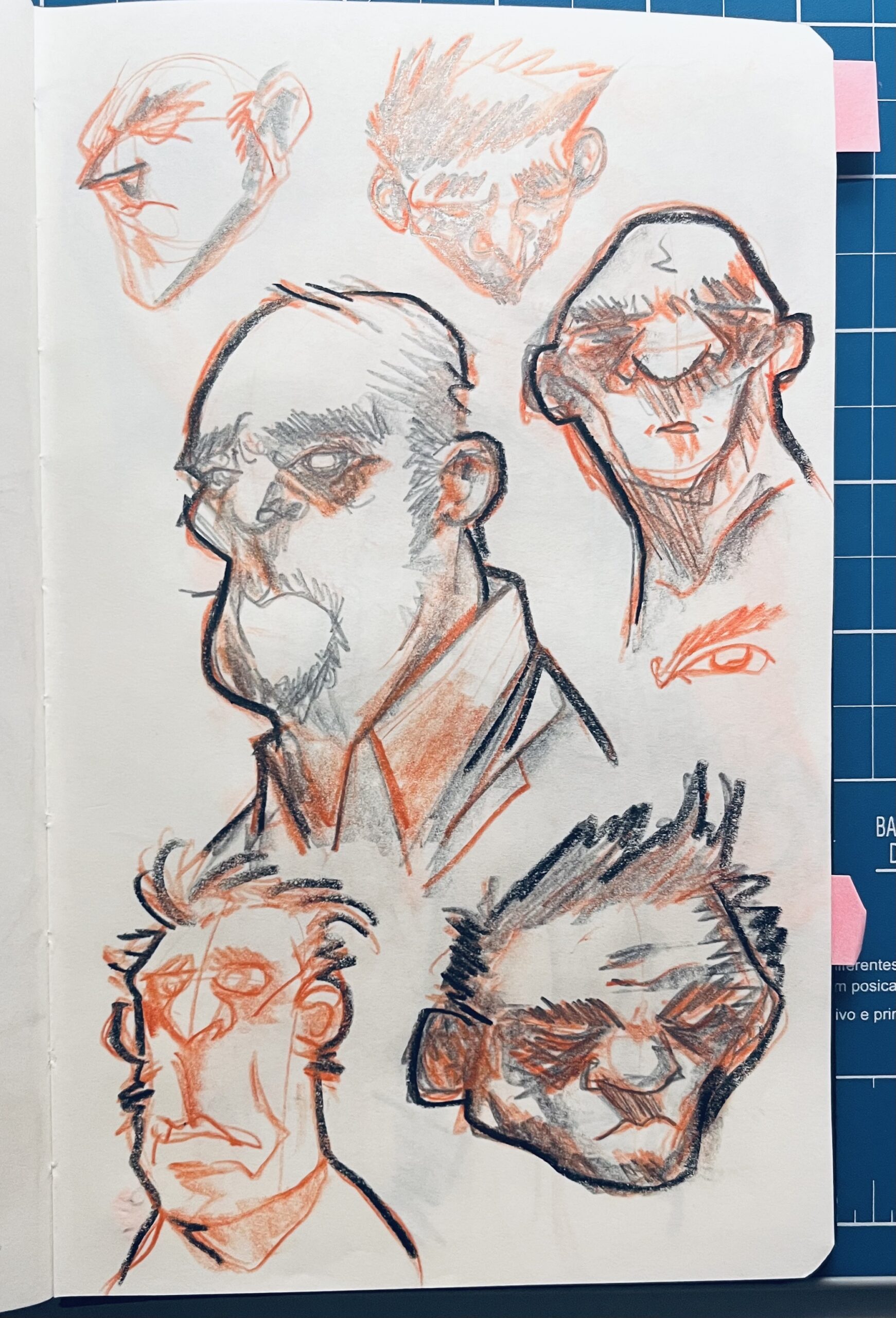 Photo of a page from a sketchbook, with a set of studies of male faces, done in red pencil.