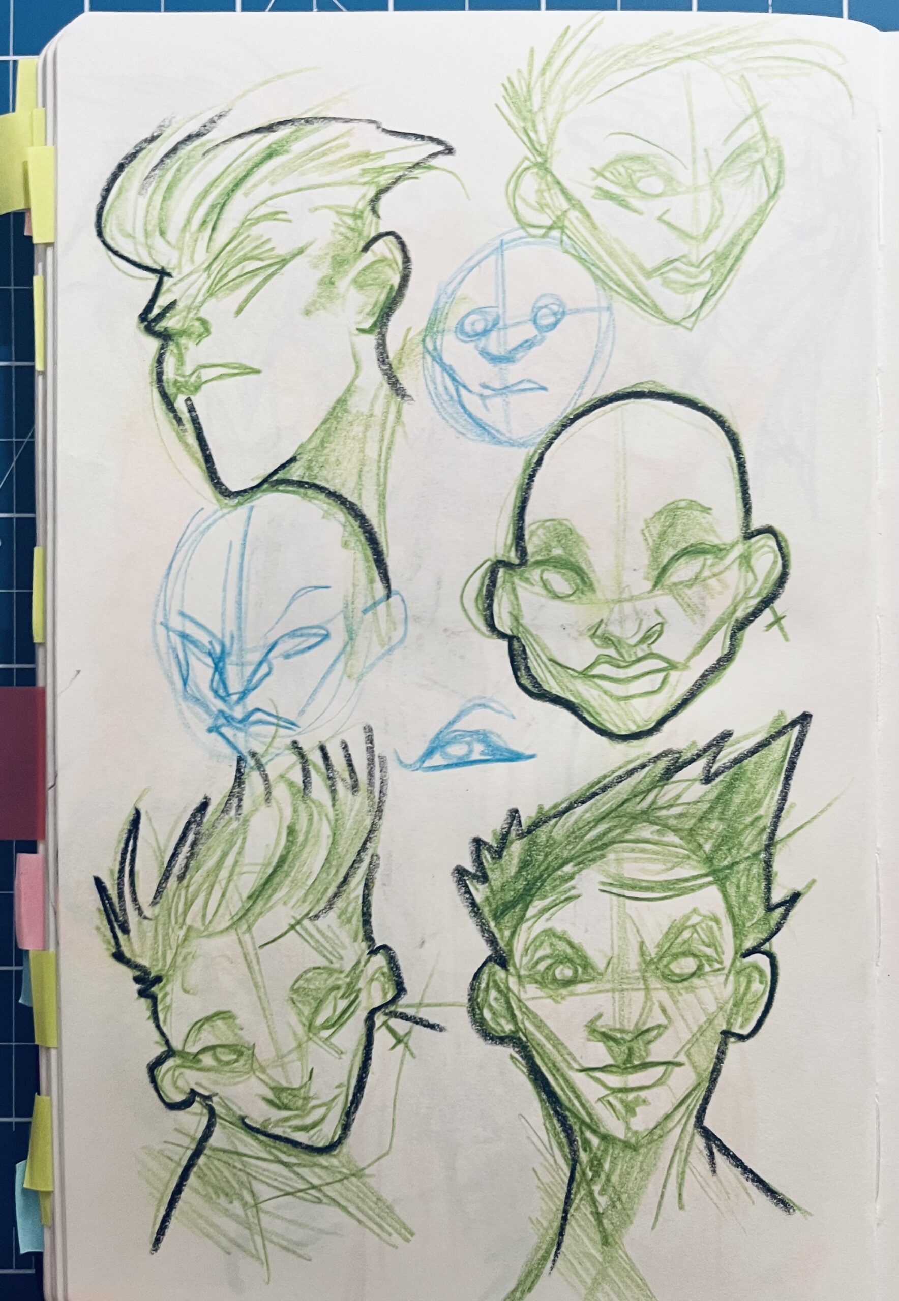 Photo of a page from a sketchbook, with a set of studies of women's faces, using green pencil.