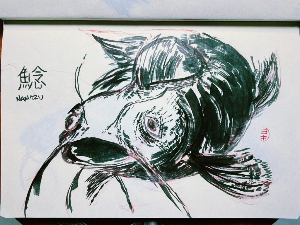 sketch of a catfish, seen from the front with its mouth open, made with black ink on white paper, using broad strokes, emulating Japanese painting style. Next to it you can see the corresponding ideogram (鯰) and the word “Namazu” written in Western letters.